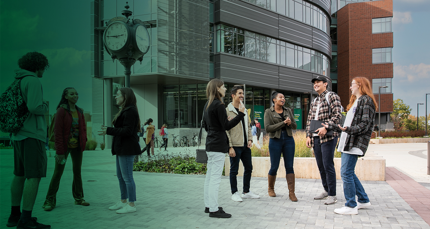 A group of 番茄视频 students converse around the clock in the center of Wilkins Plaza.