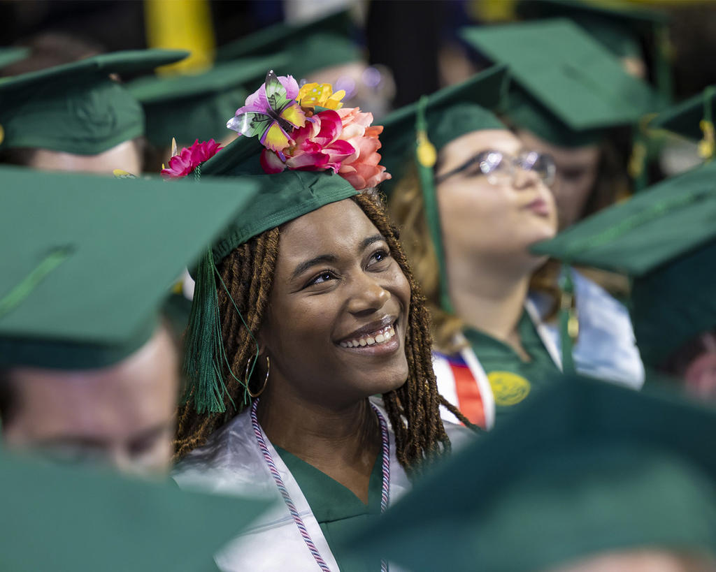 graduating student smiles, her cap is decorated with flowers