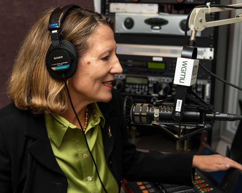 College of Public Health Dean Melissa Perry behind the mic in the podcast studio. She as she answers Mason President Gregory Washington's questions